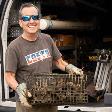 A smiling man wearing sunglasses pulls a cage full of oysters out of a van.