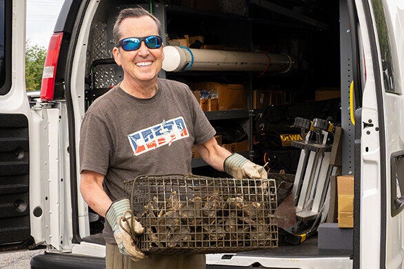 A smiling man wearing sunglasses pulls a cage full of oysters out of a van.