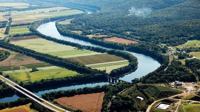 A river flanked by trees meanders through farm fields.