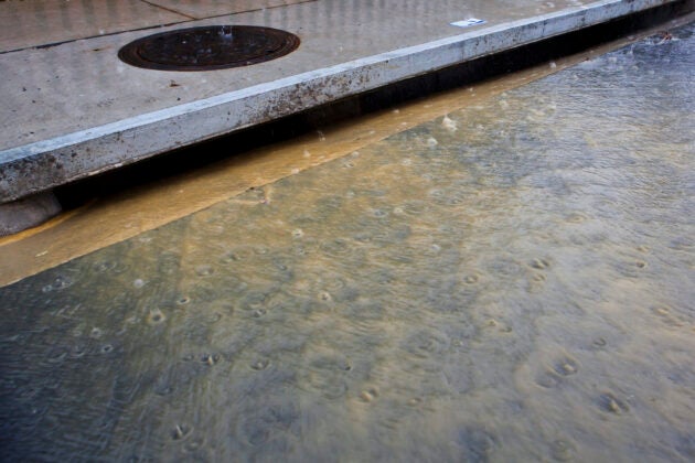 Muddy water flows into a storm drain during a rain storm.
