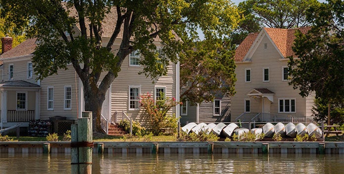 A line of canoes sits by the riverside in front of two houses.