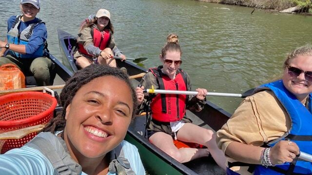 Students from the Bay Advocacy Institute paddle canoes on a sunny day, enjoying hands-on environmental education on a calm river.
