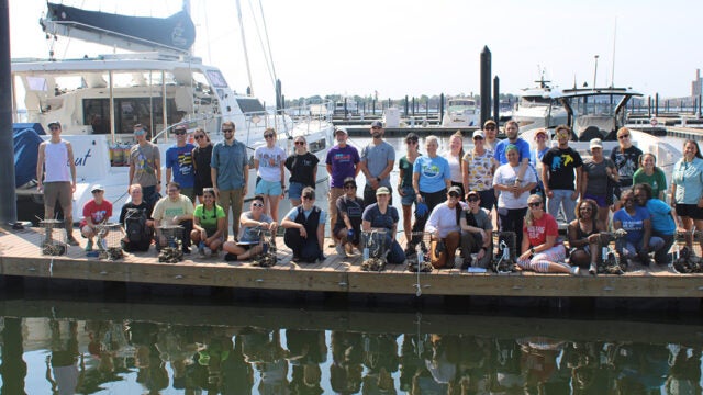 A large group of people stand on a dock, preparing to plant their oyster cages.