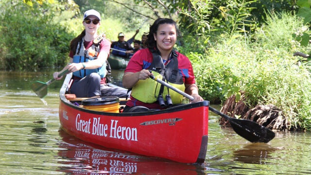 Two women paddle on a river in a red canoe.