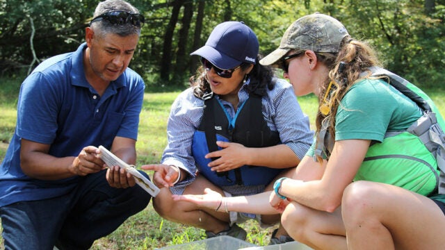 Three adults kneel to look at a fish identification card.