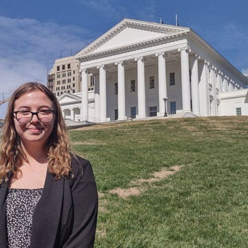 Advocate stands outside the Virginia State Capitol building on a sunny day, promoting civic engagement and environmental policy reform.