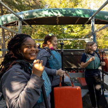 A smiling student gives a thumbs up while preparing for an outdoor education field trip with classmates.