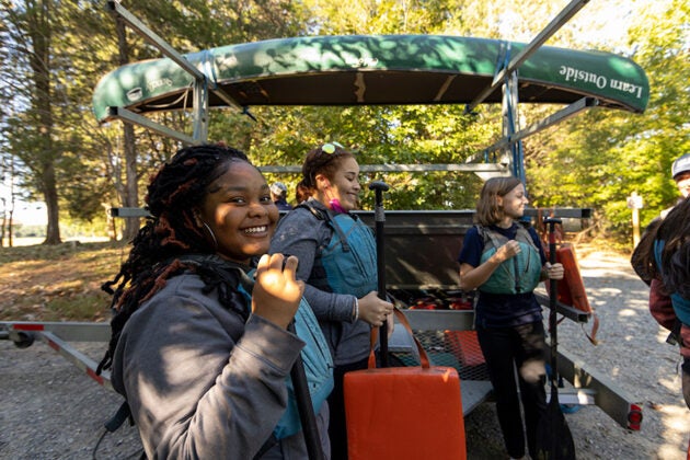 A smiling student gives a thumbs up while preparing for an outdoor education field trip with classmates.