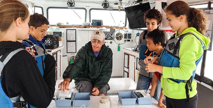 Students and an educator perform a water testing activity on a boat.