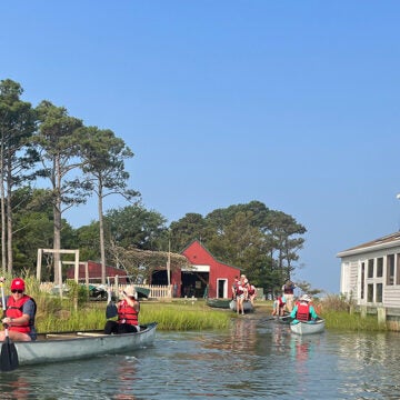 People wearing life jackets paddle in canoes and kayaks paddle on the water,