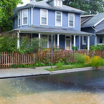 A house, with stormwater running through the street and on the sidewalks by a storm drain