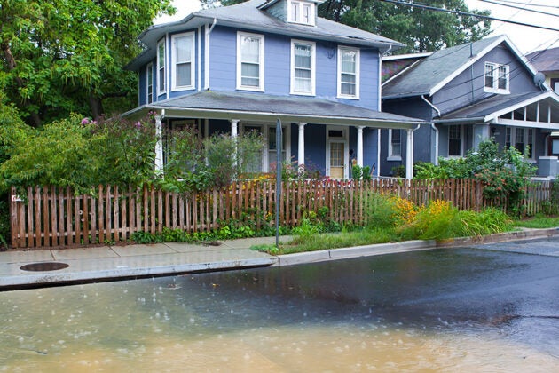 A house, with stormwater running through the street and on the sidewalks by a storm drain