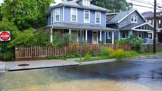 A house, with stormwater running through the street and on the sidewalks by a storm drain.