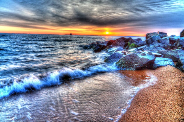 Vibrant Chesapeake Bay sunrise with waves crashing against rocky shoreline and golden light reflecting on the water.