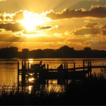Silhouetted dock on the Chesapeake Bay at sunrise with golden light breaking through dramatic clouds and reflecting on calm water