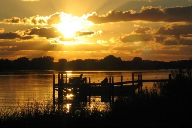 Silhouetted dock on the Chesapeake Bay at sunrise with golden light breaking through dramatic clouds and reflecting on calm water
