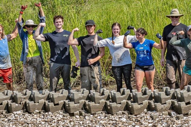 A volunteers group celebrates while standing behind a row of oyster castles.