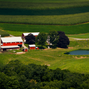 Aerial view of a farm with red barns, a silo, farmhouse, and pond surrounded by rolling agricultural fields.