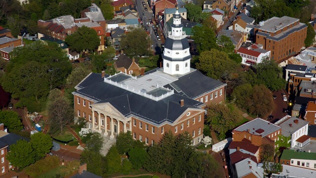 Aerial view of the Maryland State House with its white dome, surrounded by historic Annapolis buildings and green trees.