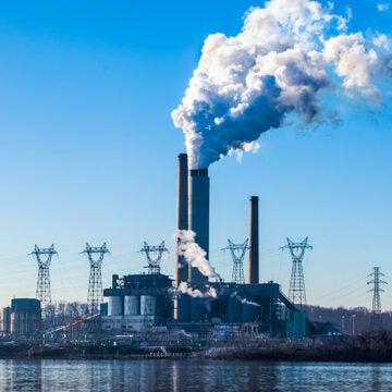 A power plant across a stretch of water, with several towers emitting clouds into the air