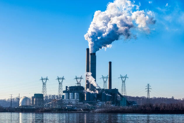 A power plant across a stretch of water, with several towers emitting clouds into the air