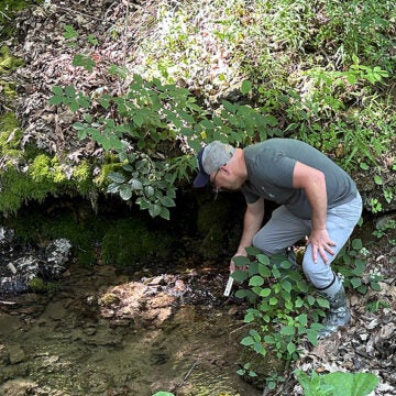 A man kneels next to a small stream.