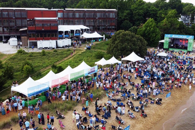An aerial view of a crowded beach with white tents and a stage.