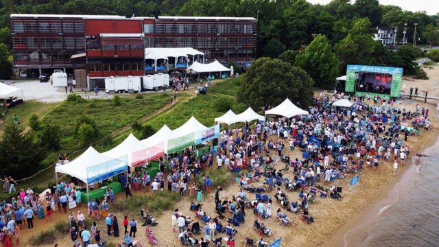 An aerial view of a crowded beach with white tents and a stage.