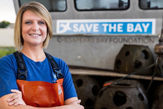A woman with short blond hair and orange waders stands on the deck of a boat.