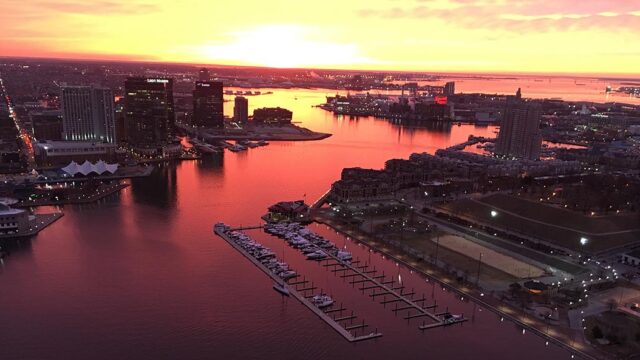 Aerial view of the Baltimore Inner Harbor at sunrise in dramatic orange light.
