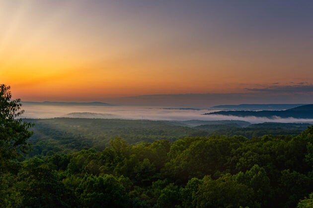 Sunrise over forested mountains with fog settling in the valleys below.