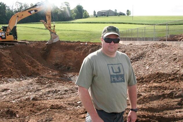 A man in sunglasses and a cap stands in front of construction excavation equipment