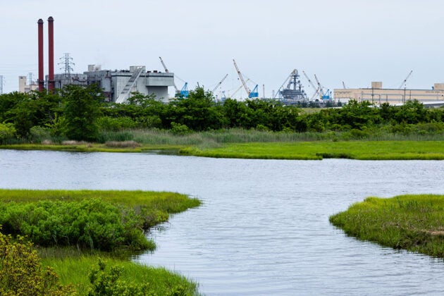 Creek running through wetlands with industrial factories in the background.
