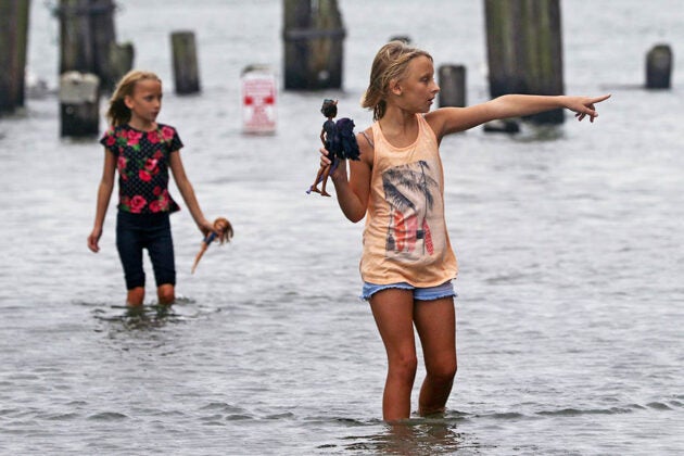 Two young girls holding dolls stand in floodwaters