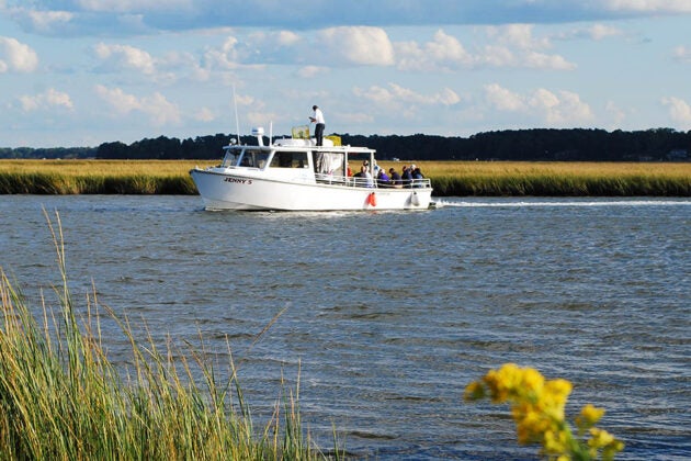 A boat named Jenny S motors through the water with golden marsh grasses along the shoreline.