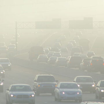 Heavy traffic on a highway shrouded in thick smog and air pollution with reduced visibility.