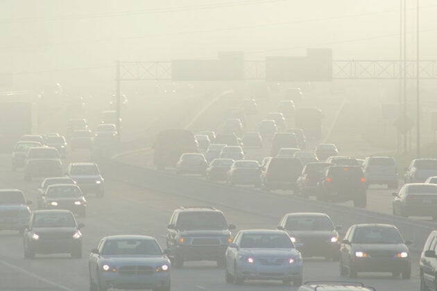 Heavy traffic on a highway shrouded in thick smog and air pollution with reduced visibility.