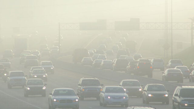 Heavy traffic on a highway shrouded in thick smog and air pollution with reduced visibility.