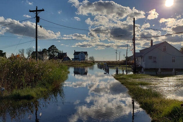 High tide flooding covers a residential street on Smith Island with houses reflected in the water and dramatic clouds overhead.