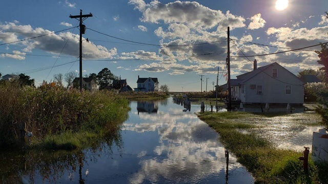 High tide flooding covers a residential street on Smith Island with houses reflected in the water and dramatic clouds overhead.