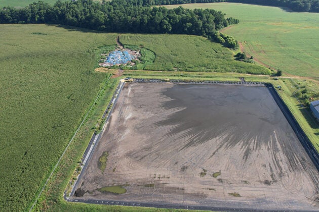 Aerial view of a large rectangular wastewater lagoon surrounded by green agricultural fields and farm buildings.