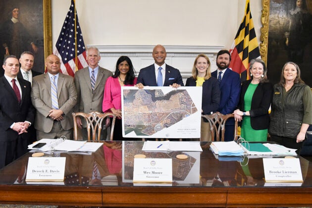 Maryland Governor Wes Moore and a group of officials stand behind a table displaying a map of Holly Beach Farm.