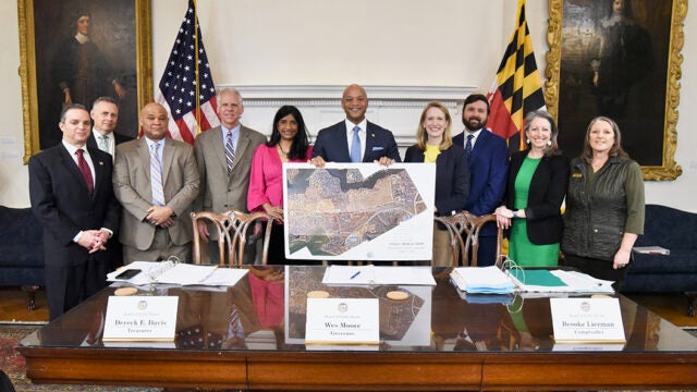 Maryland Governor Wes Moore and a group of officials stand behind a table displaying a map of Holly Beach Farm.