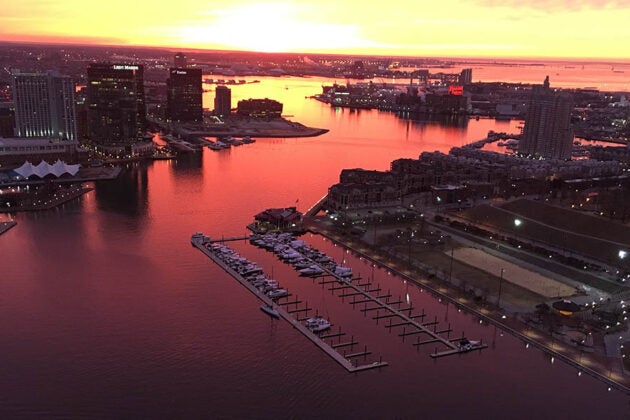 Aerial view of the Baltimore Inner Harbor at sunset with the orange sky reflected in the water.