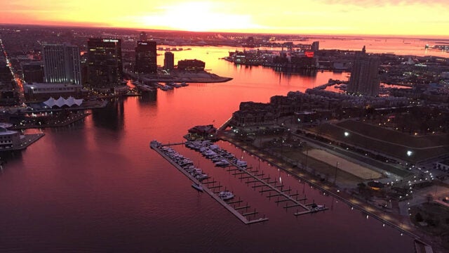 Aerial view of the Baltimore Inner Harbor at sunset with the orange sky reflected in the water.